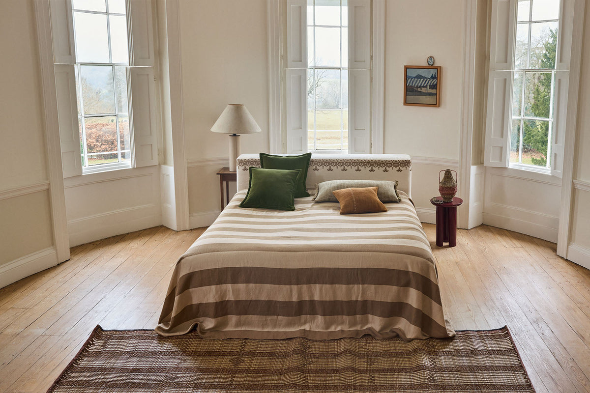 Wide width linen stripe in honey and natural on a bed in front of a large bay window.