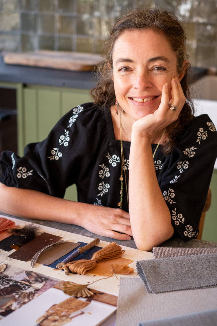 Woman sitting at a table with fabric samples, smiling.