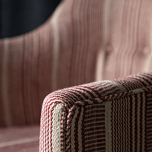 Close-up of a striped upholstered armchair corner, showing textured woven fabric in muted red, beige, and brown tones.