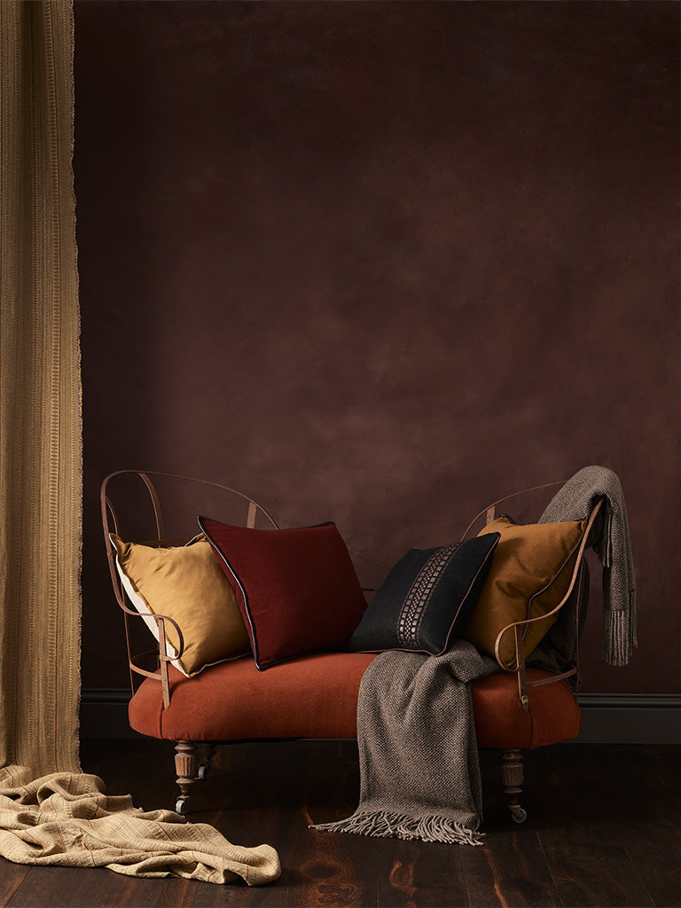 Decorative setup with a red chair, cushions, and blankets against a dark wall.
