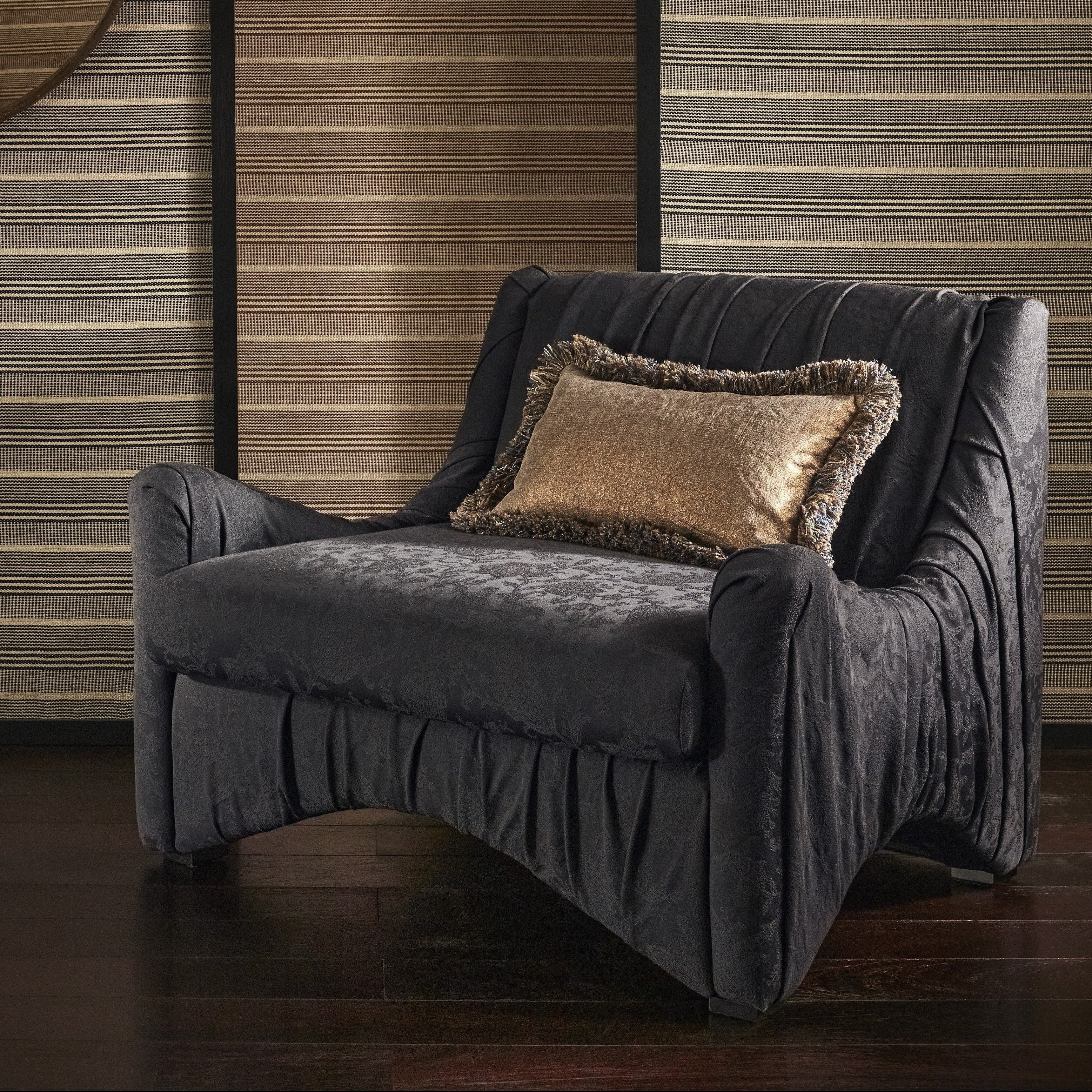 Navy armchair with a decorative pillow against a wooden panelled wall.