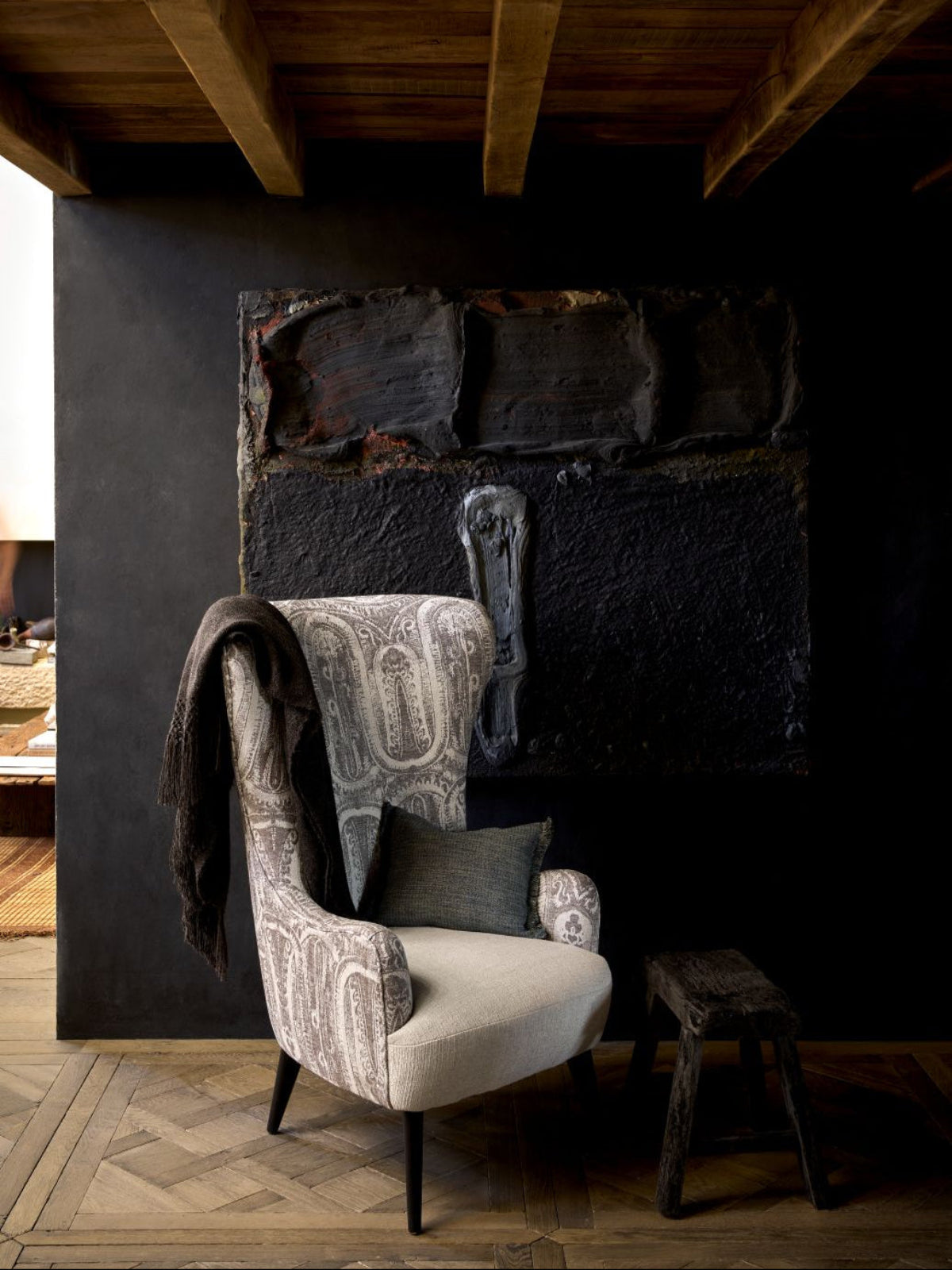 Decorative armchair with patterned fabric against a dark wall with stone-like texture.