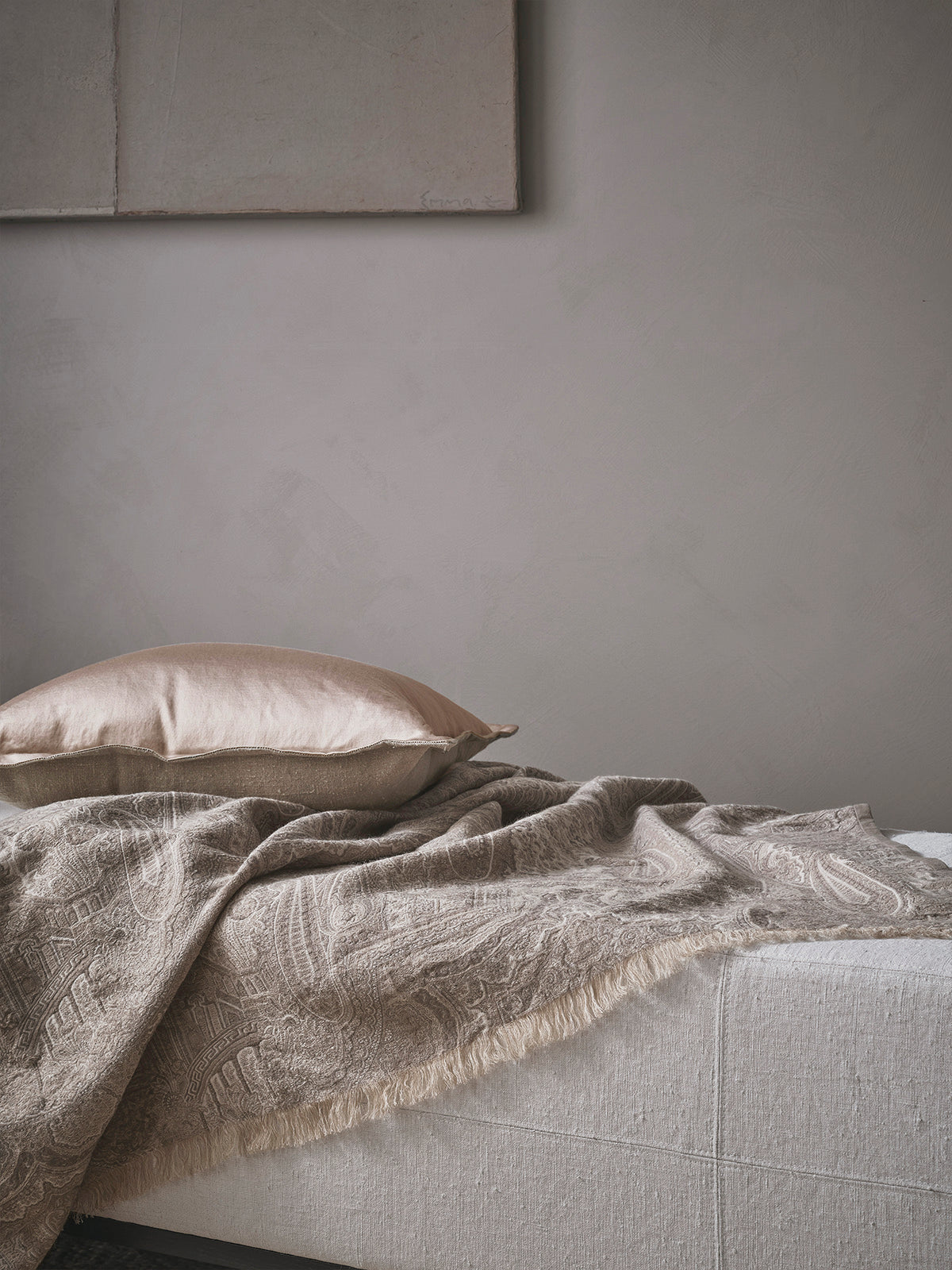 Textured blanket and cushion on a sofa against a grey wall.