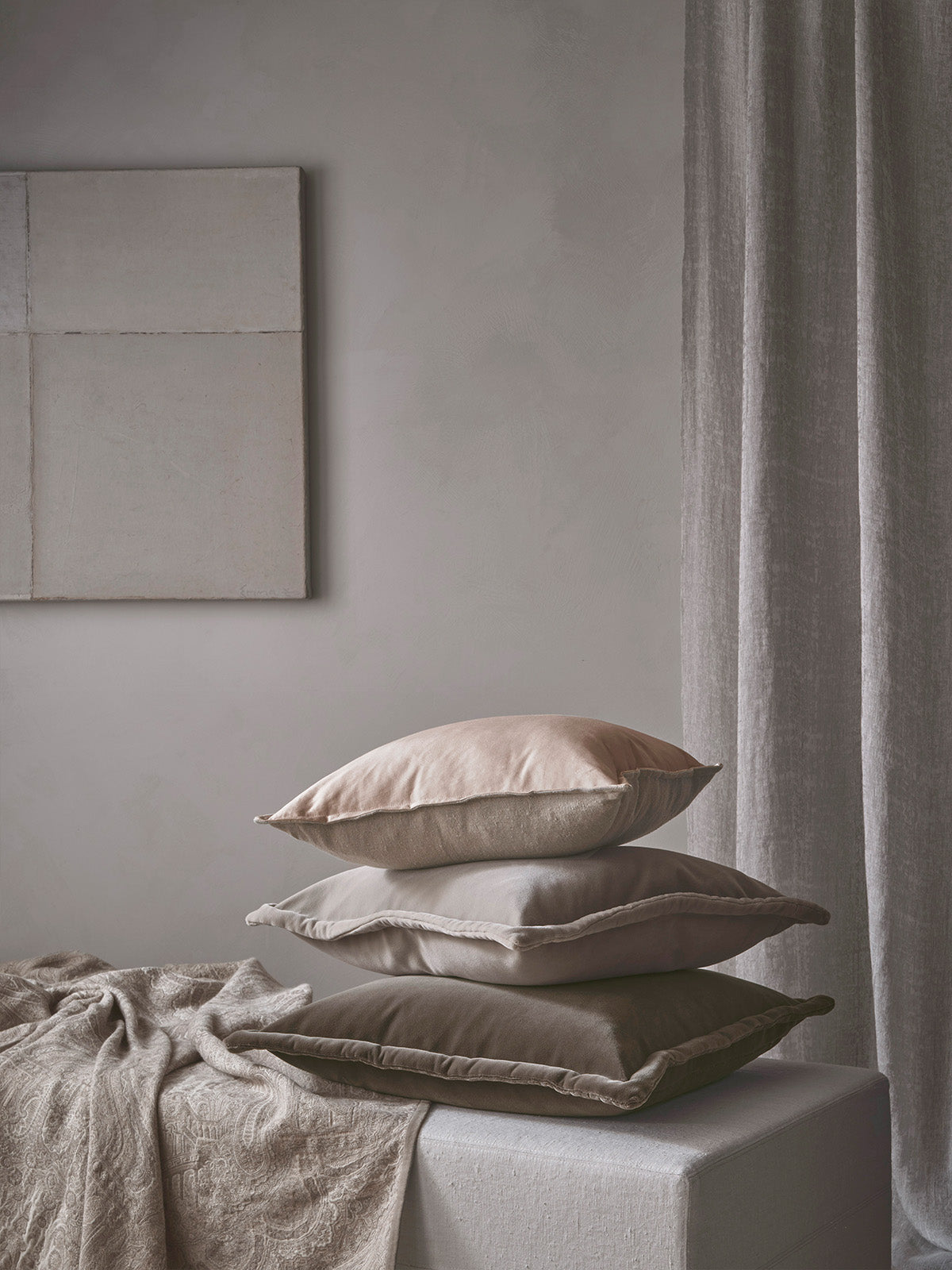 Stack of beige cushion on a bed with a neutral colour scheme.