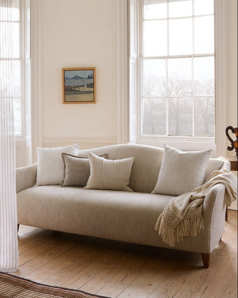 Beige sofa in a living room with large windows and a framed picture on the wall.