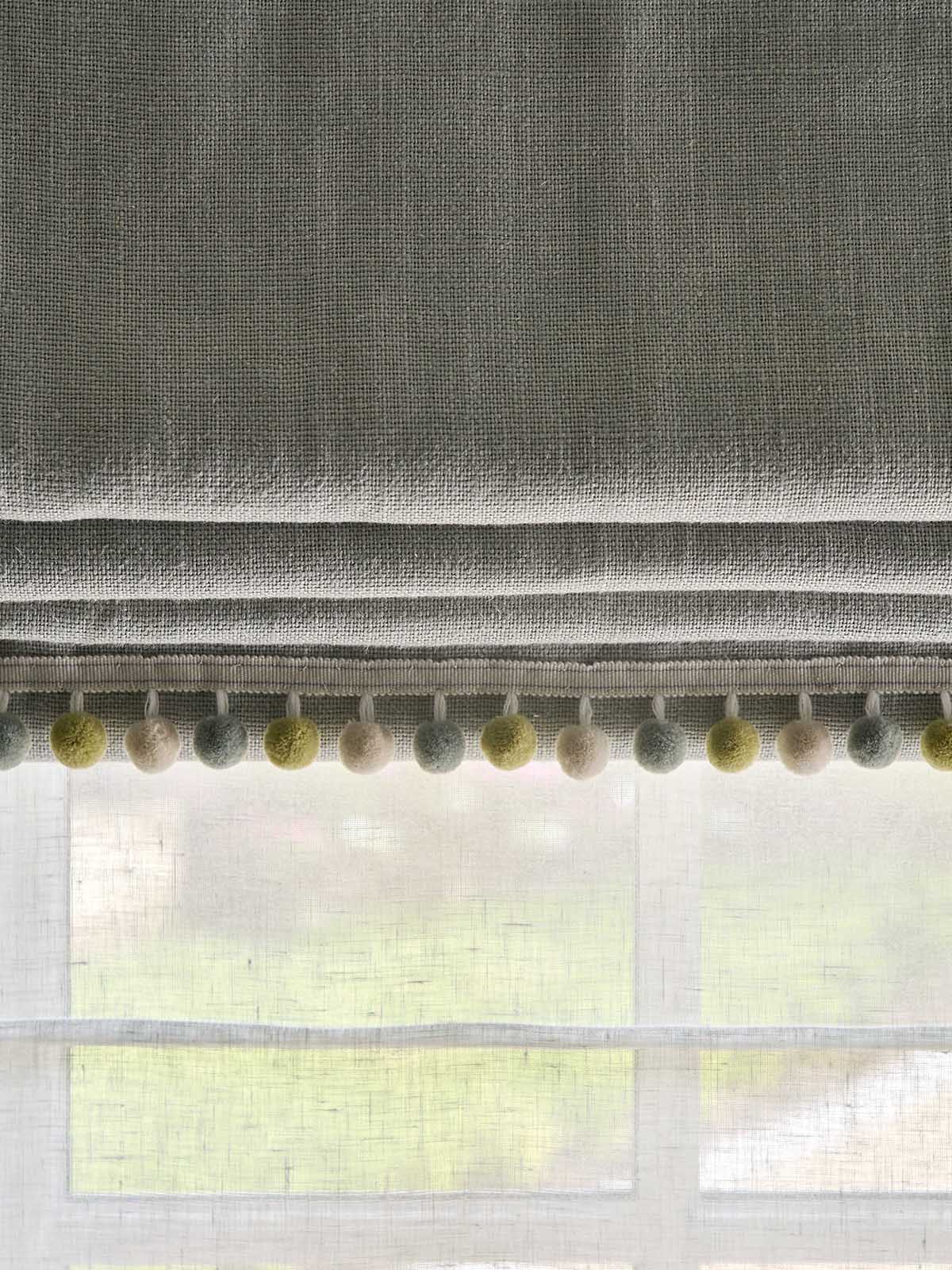 Textured gray curtain with colorful pom-pom trim in front of a window.