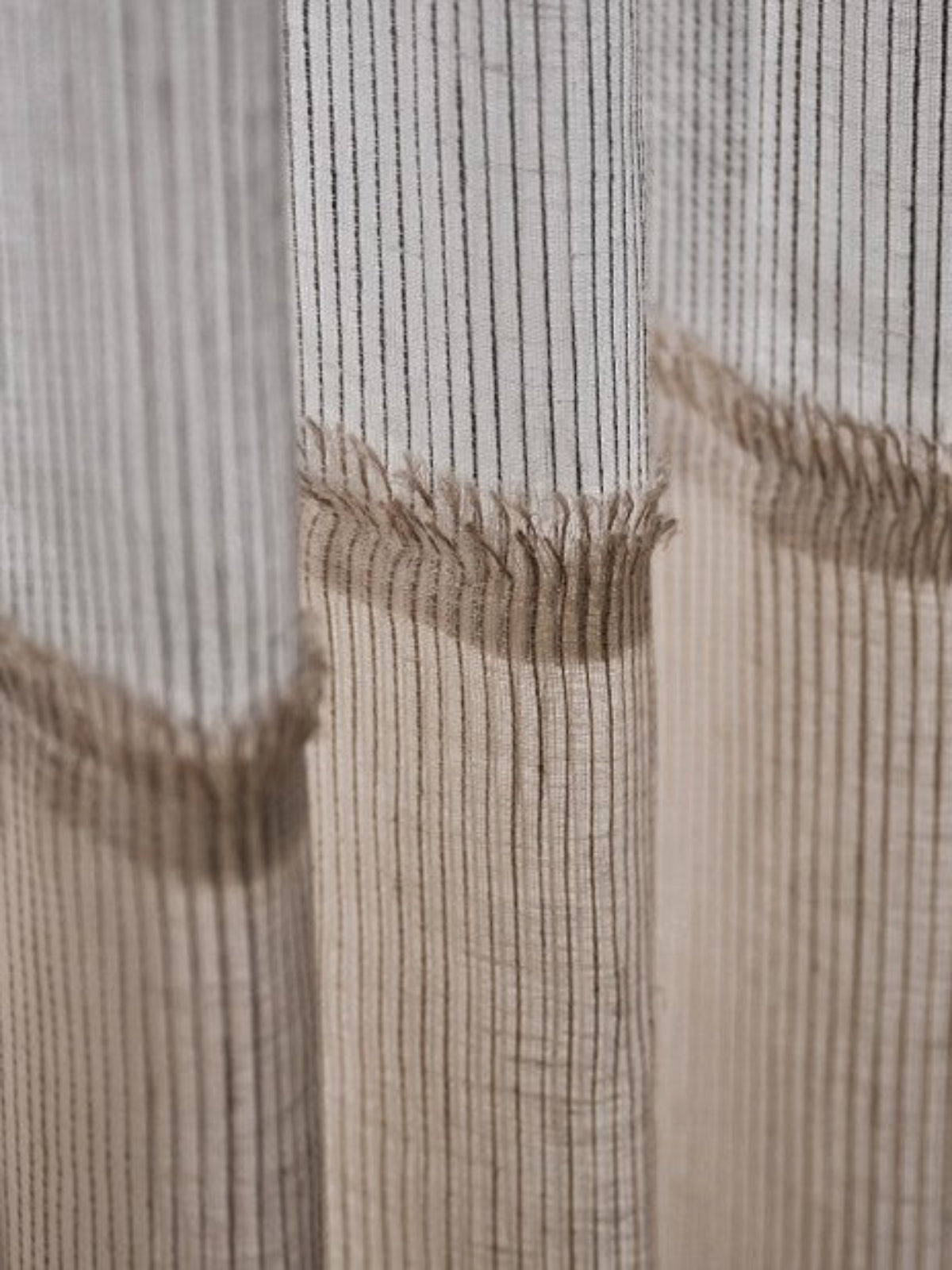 Close-up of a textured curtain panel with vertical ribbed stripes in beige and off-white, featuring a frayed hem.