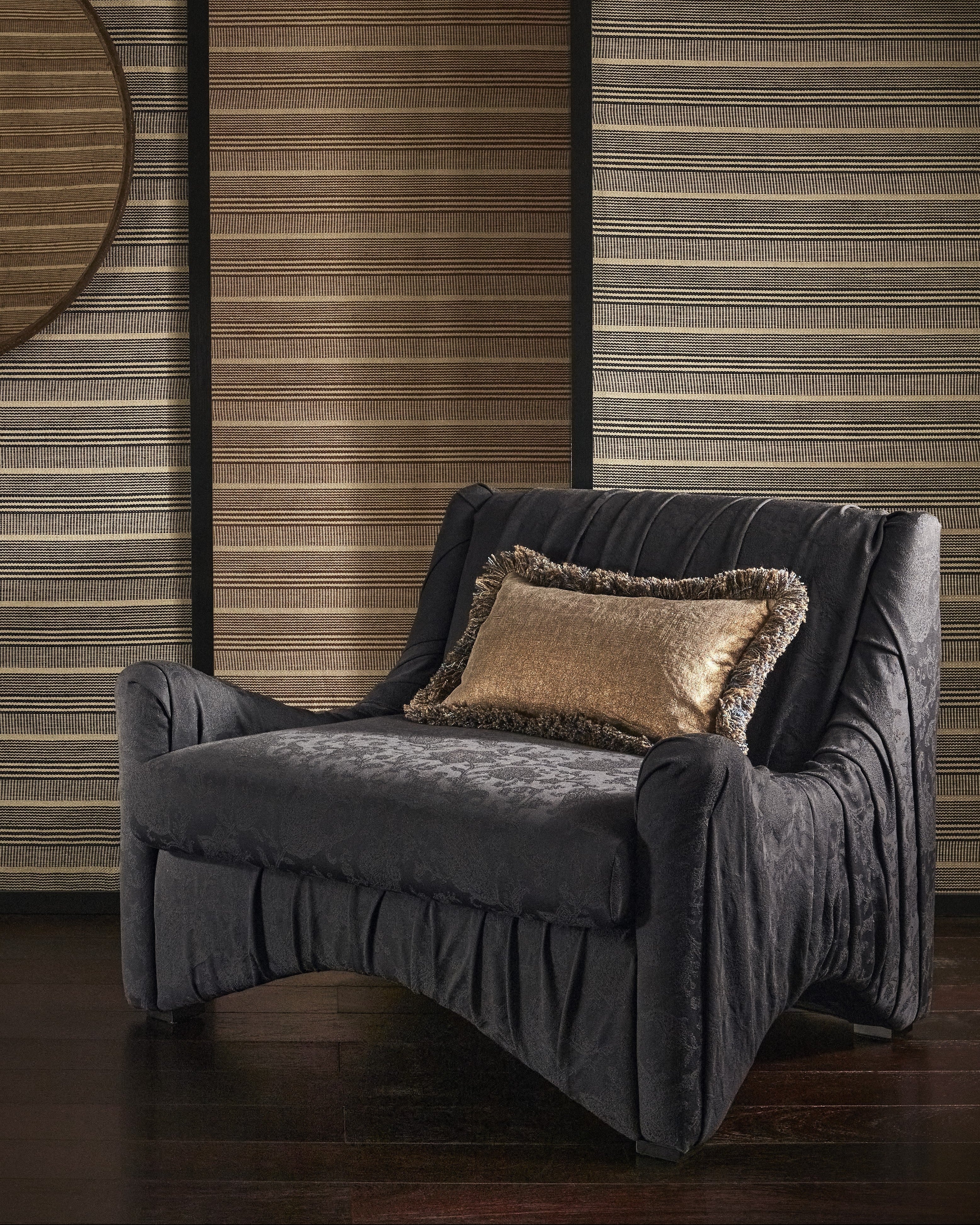 Navy armchair with a decorative pillow against a wooden panelled wall.