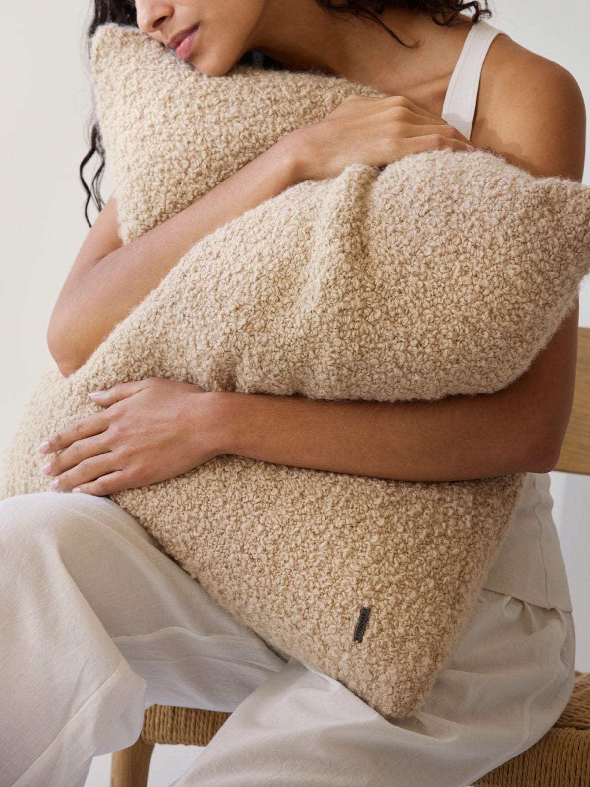 Woman holding two beige textured cushions with a visible brand logo.