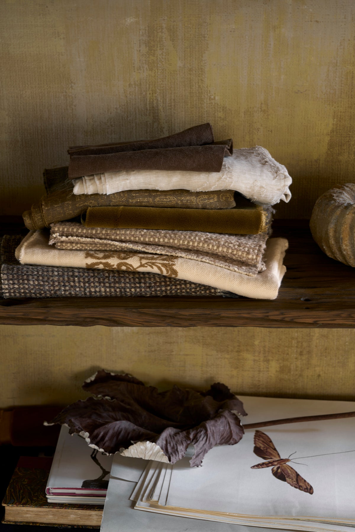 Stack of folded fabric on a wooden shelf with a textured wall background